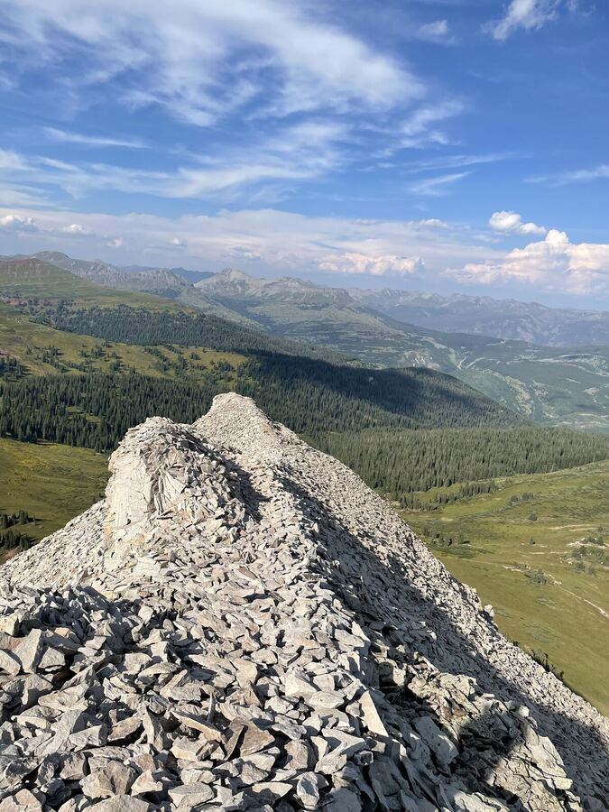 A pale rock crest above wide green valleys, clouds across the sky