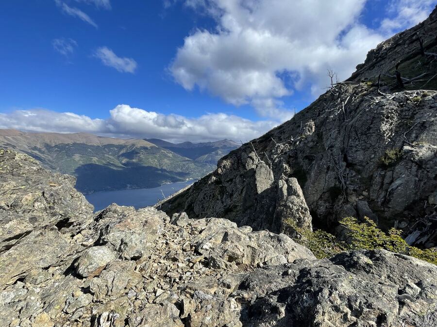 A grey granite outcrop above a lake, clouds billowing over the range