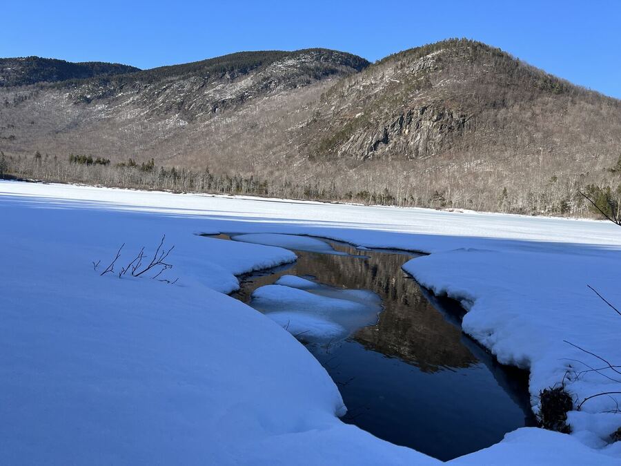 Dark open water in a snowy pond, hills beyond