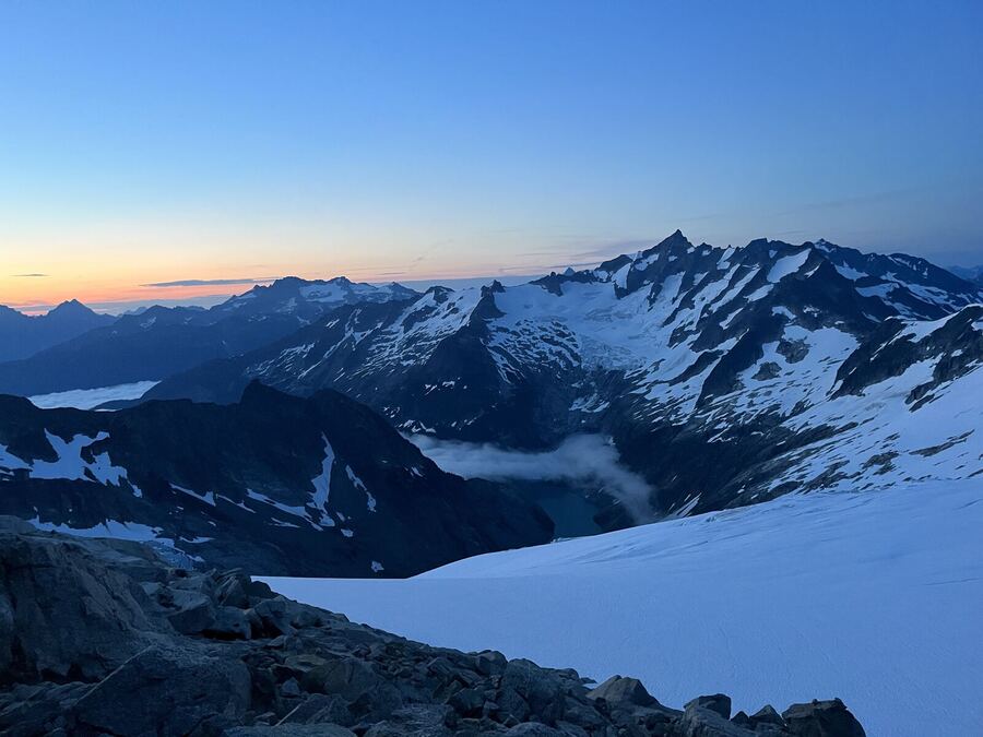Dawn light behind a snowy range, a glacier in front
