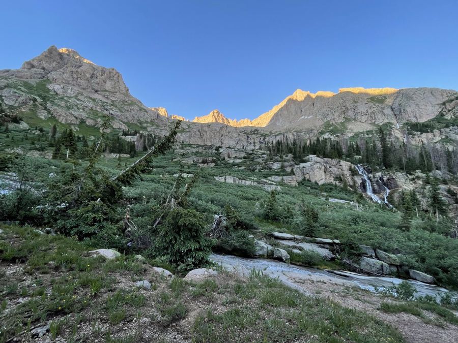 Last light on a rock rim above a meadow, with a small waterfall spilling over slabs