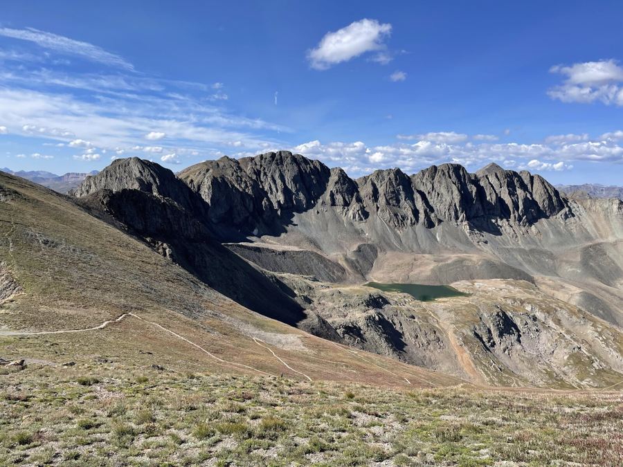A jagged dark ridge above a small green lake, a trail crossing the tundra in the foreground