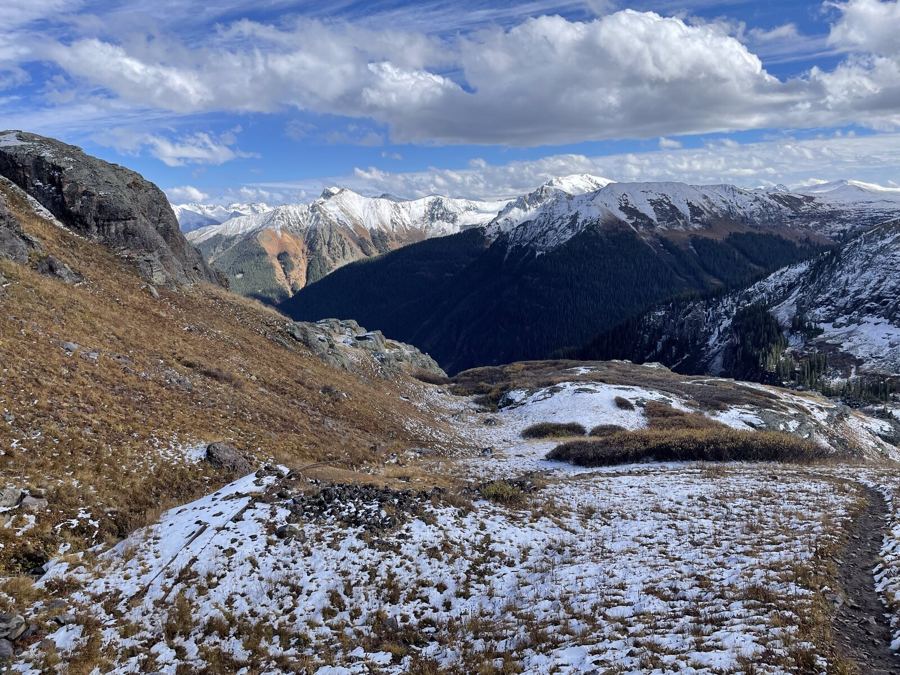 Fresh snow on a high bench, red and white mountains beyond under a cloud bank