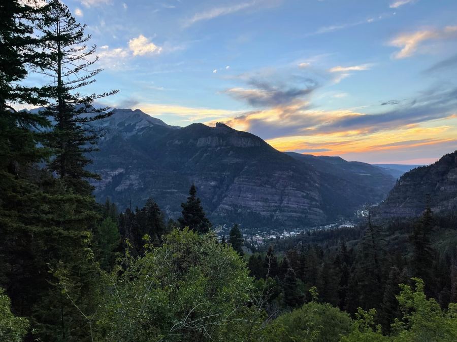 Sunset colour over a canyon, dark ridges and fir trees in silhouette